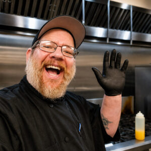 Table Ready Meal Prep's head Chef Brandon Waugh in a commercial kitchen with a big smile and wave.