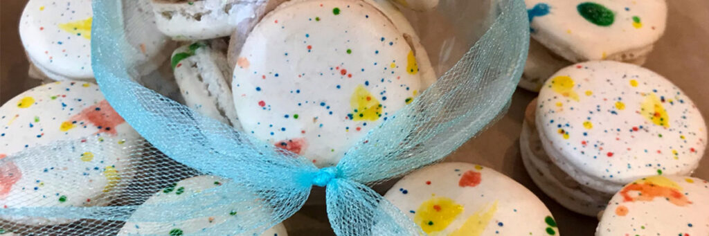 
Colorful confetti macarons with sprinkles and a blue ribbon bow, handmade by Artisan Sweets Bakery Bixby, OK 